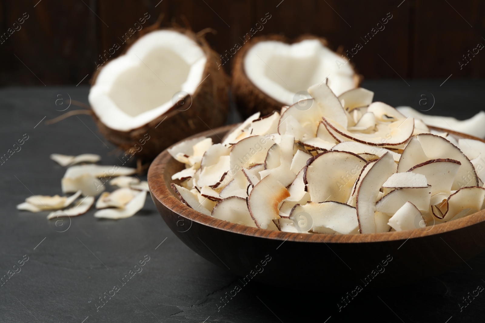 Photo of Tasty coconut chips in bowl on black table