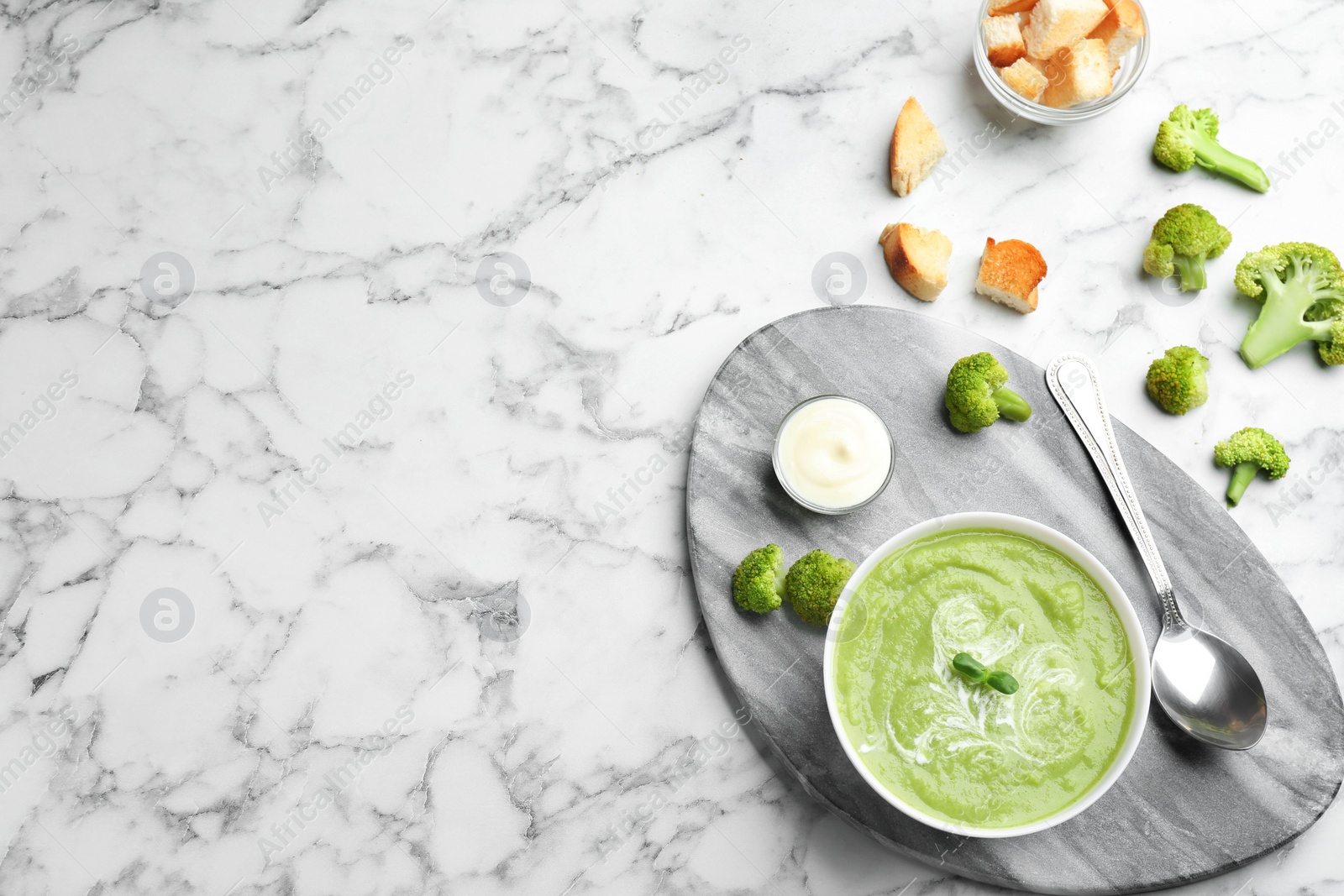 Photo of Flat lay composition with bowl of broccoli cream soup on white marble table, space for text