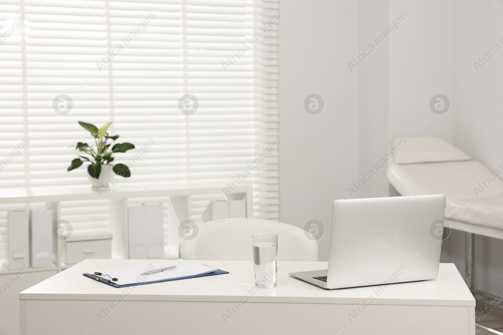 Photo of Doctor's workplace. Laptop, clipboard and glass of water on white table in hospital