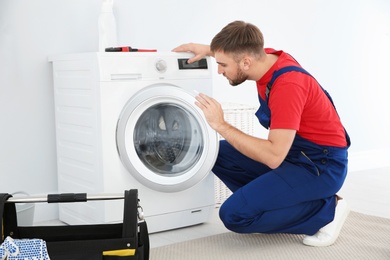 Photo of Young plumber examining washing machine in bathroom