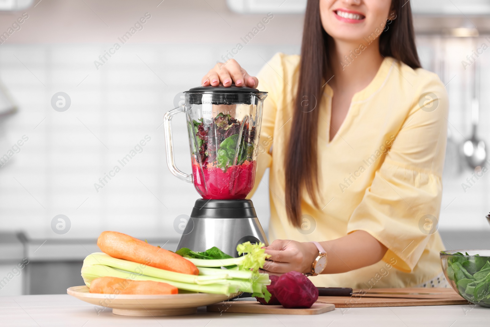 Photo of Young woman preparing tasty healthy smoothie at table in kitchen