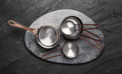 Photo of Saucepans and marble board on black table, flat lay. Cooking utensils