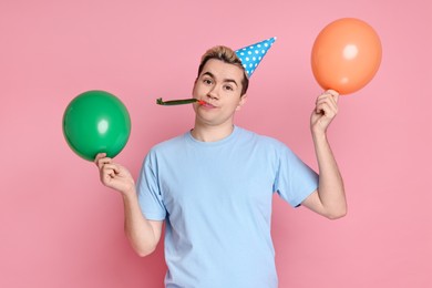 Young man with party hat, balloons and blower on pink background