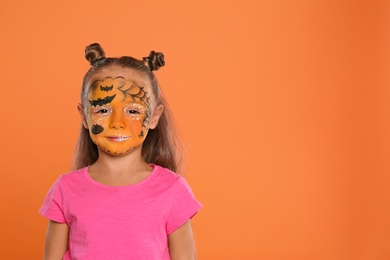 Cute little girl with face painting on orange background. Space for text
