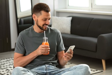 Photo of Man with bottle of delicious juice and smartphone at home
