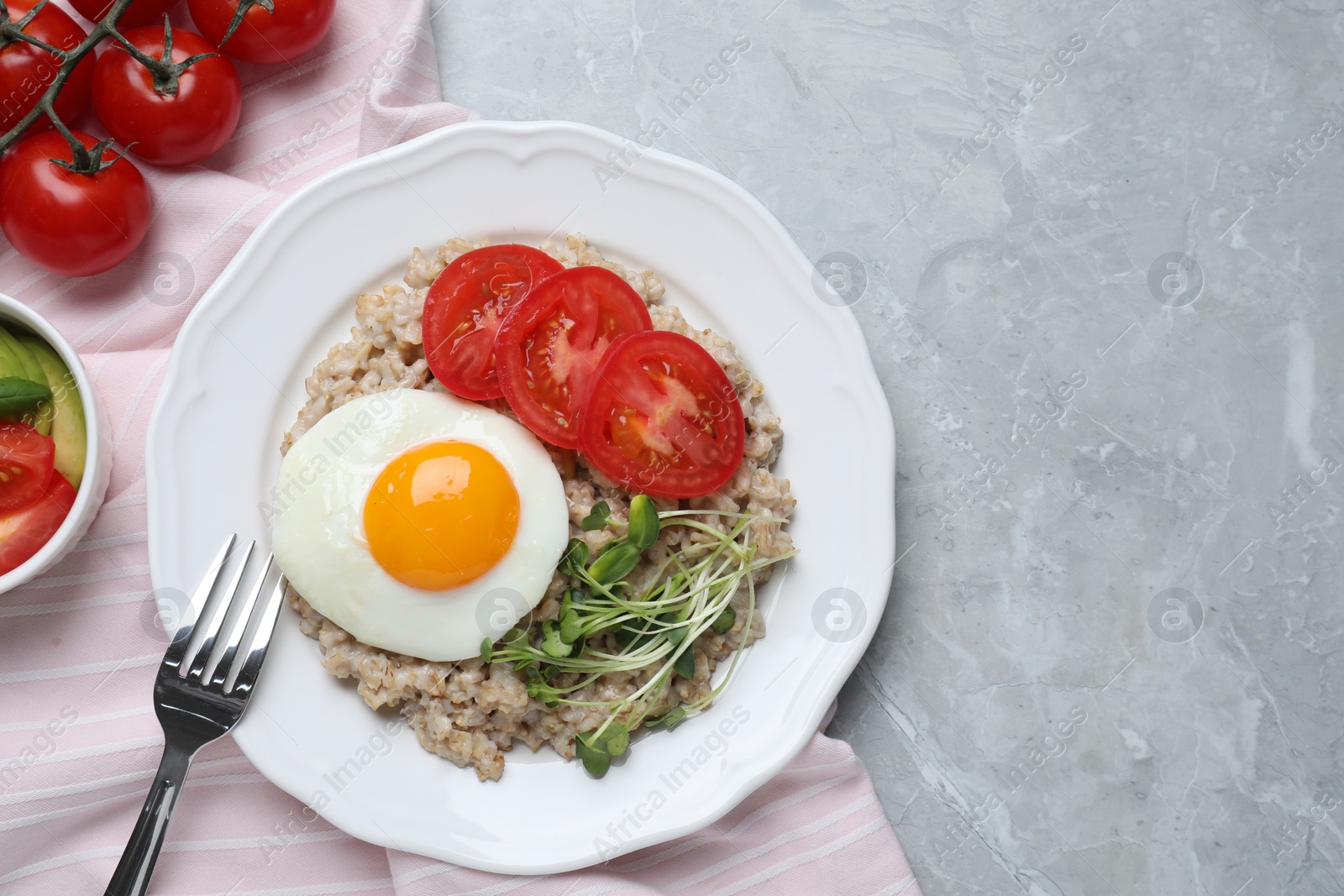 Photo of Delicious boiled oatmeal with fried egg, tomatoes and microgreens on light grey marble table, flat lay. Space for text