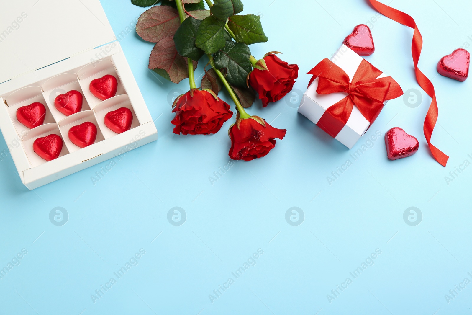 Photo of Heart shaped chocolate candies, gift box and bouquet on light blue background, flat lay. Space for text