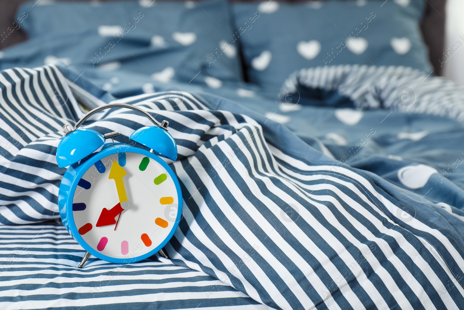 Photo of Analog alarm clock on bed. Time of day