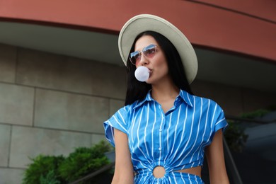 Stylish woman blowing gum near building outdoors