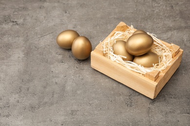 Wooden crate with golden eggs on table, space for text