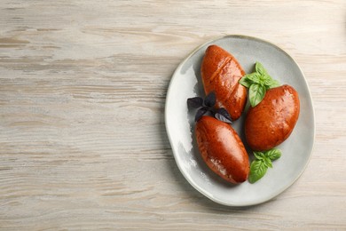 Delicious baked pirozhki and basil on wooden table, top view. Space for text