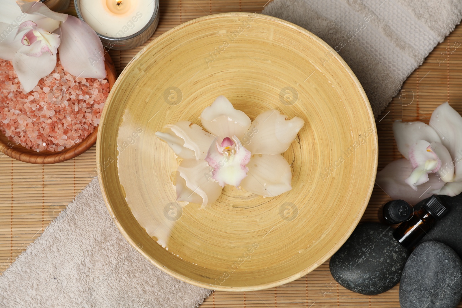 Photo of Bowl with water and flowers on bamboo mat, flat lay. Spa treatment