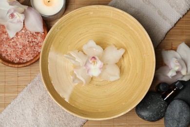 Bowl with water and flowers on bamboo mat, flat lay. Spa treatment
