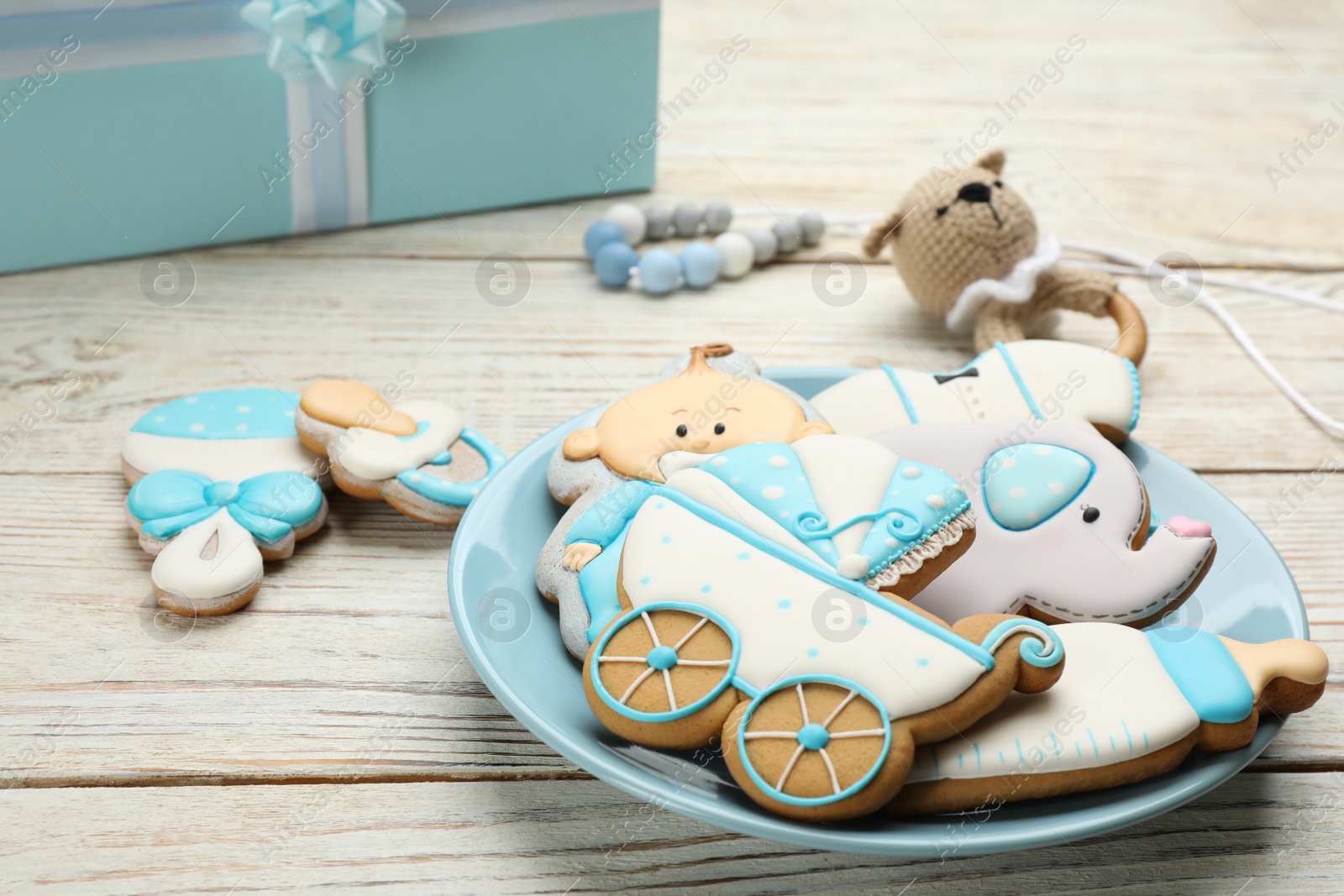 Photo of Plate of baby shower cookies and accessories on white wooden table