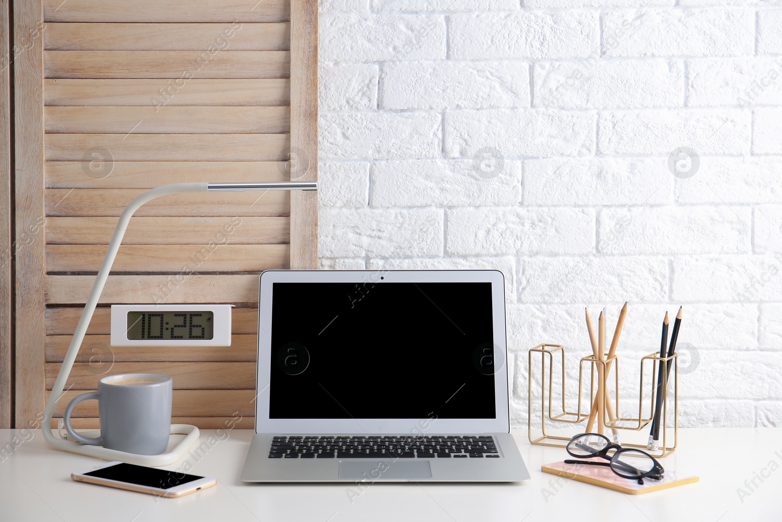 Photo of Modern workplace with laptop on table against brick wall. Mockup for design