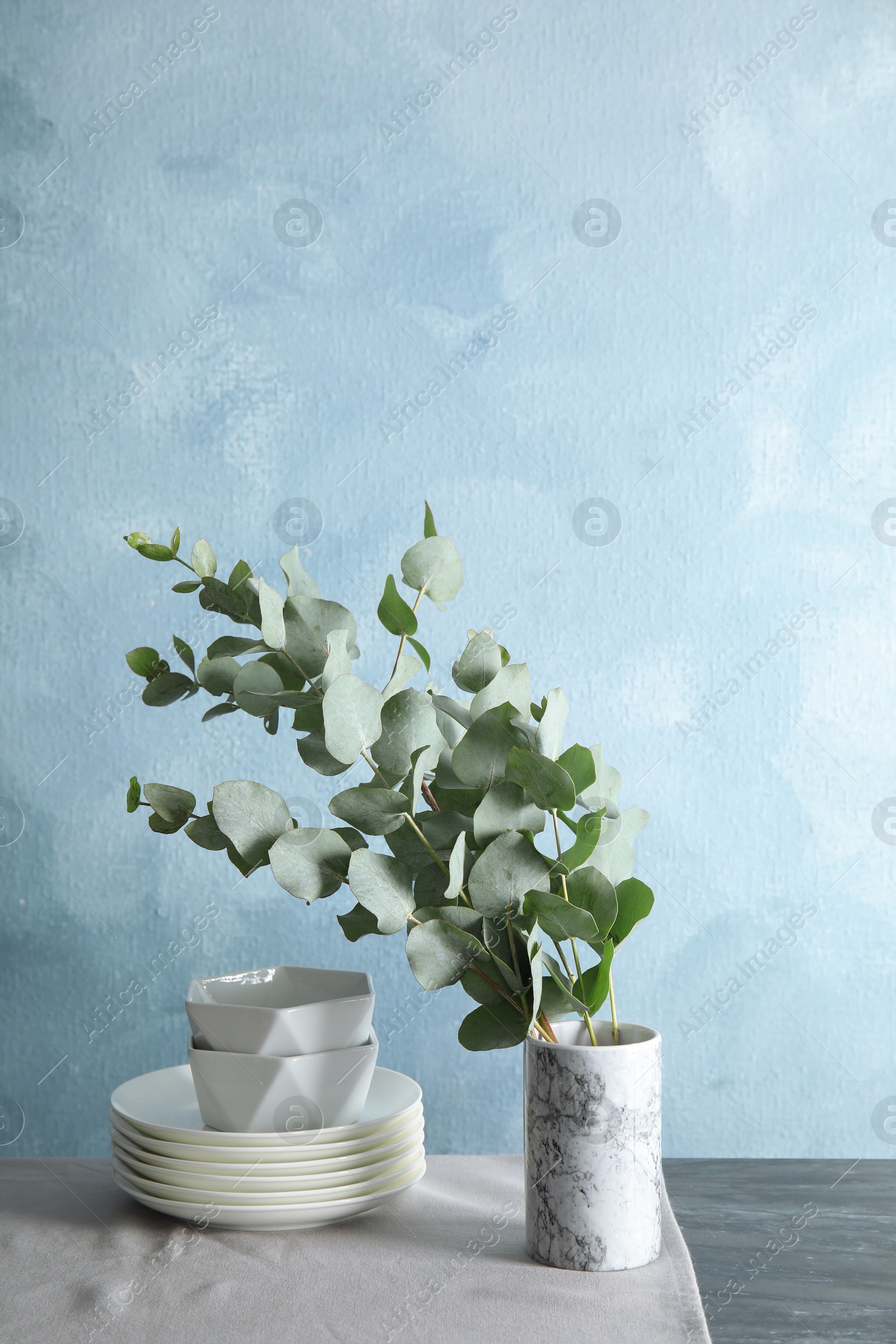 Photo of Bunch of eucalyptus branches with fresh leaves in vase and dishware on table