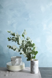 Photo of Bunch of eucalyptus branches with fresh leaves in vase and dishware on table