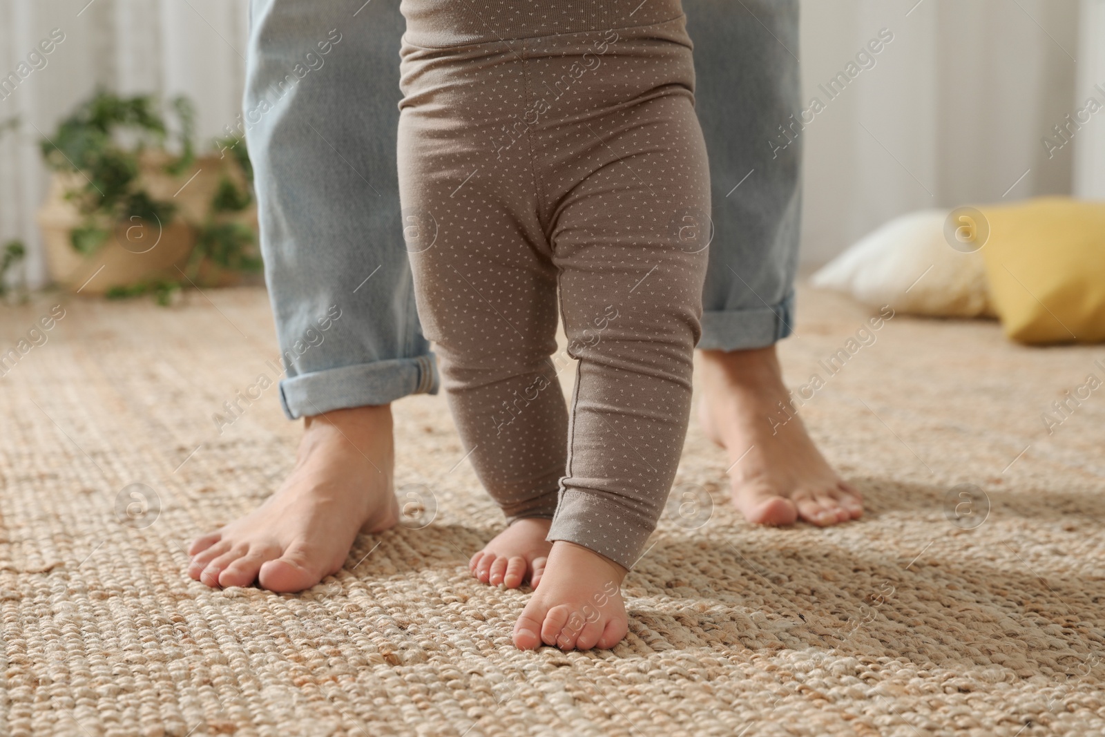 Photo of Mother supporting her baby daughter while she learning to walk at home, closeup