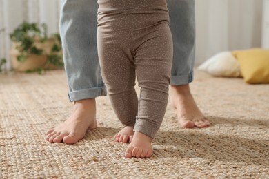 Photo of Mother supporting her baby daughter while she learning to walk at home, closeup