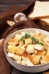 Delicious crispy croutons with rosemary in bowl on table, closeup