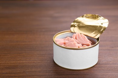 Photo of Tin can with canned tuna on wooden table, closeup. Space for text
