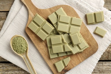 Photo of Pieces of tasty matcha chocolate bar and powder in spoon on wooden table, top view