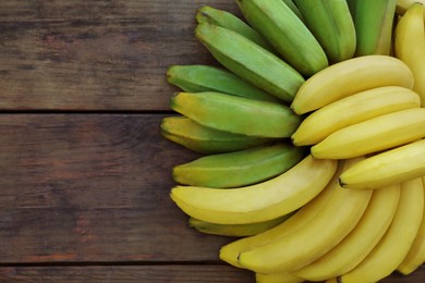 Photo of Bunches of tasty bananas on wooden table, flat lay. Space for text