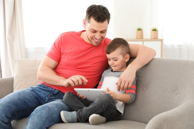 Photo of Boy and his father with tablet sitting on sofa at home. Family time