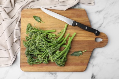 Photo of Fresh raw broccolini and knife on white marble table, flat lay. Healthy food