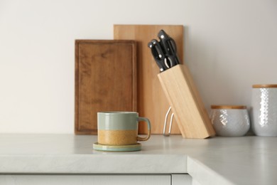 One ceramic mug with coaster on light countertop in kitchen