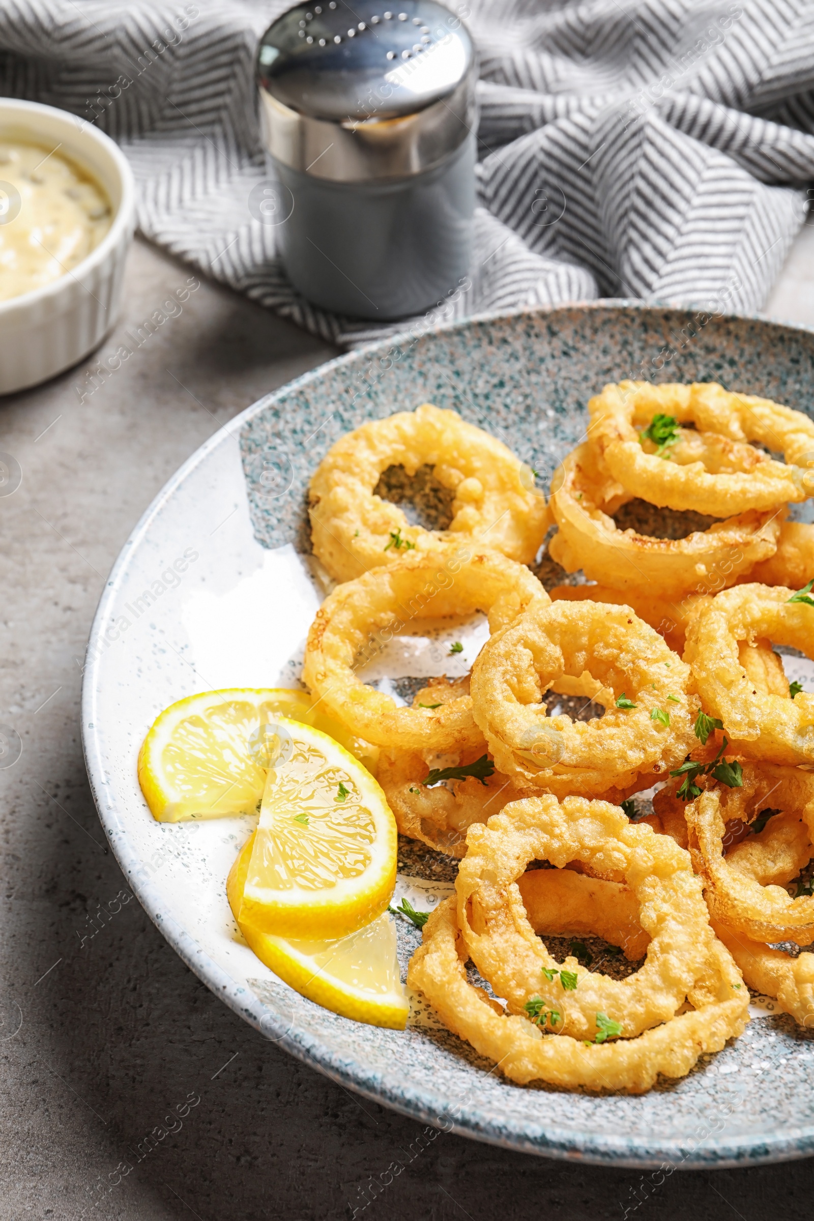 Photo of Plate with homemade crunchy fried onion rings and lemon slices on table, closeup