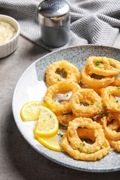 Photo of Plate with homemade crunchy fried onion rings and lemon slices on table, closeup