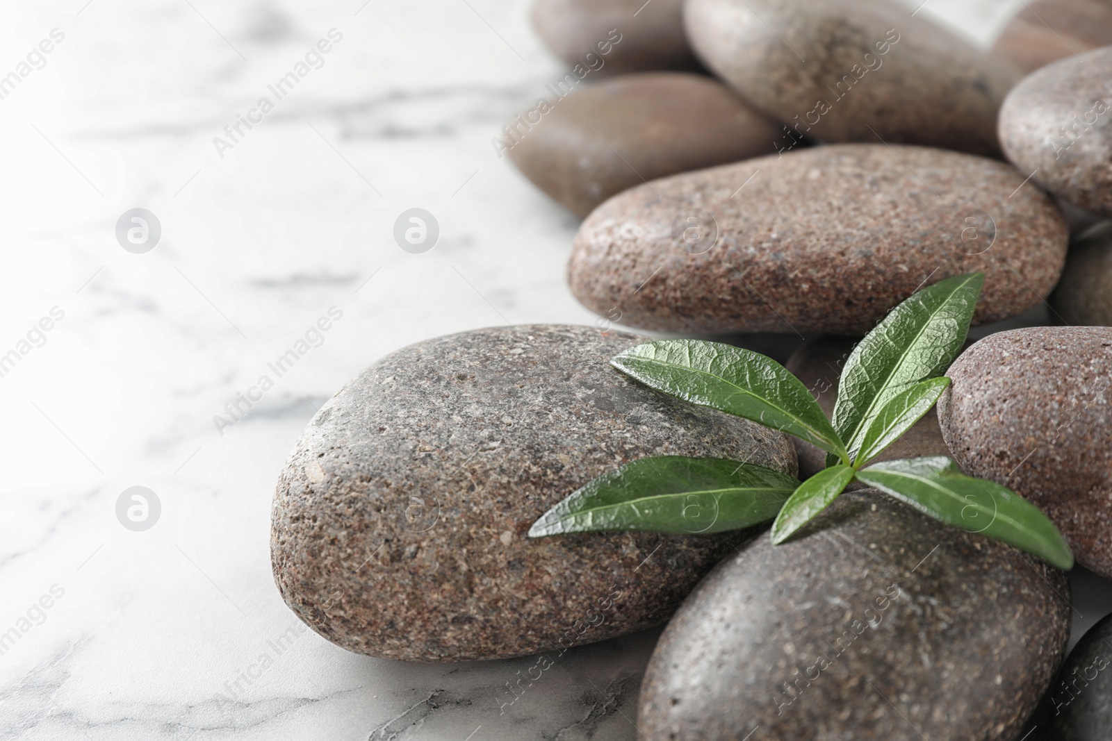 Photo of Spa stones and green leaves on marble table, space for text