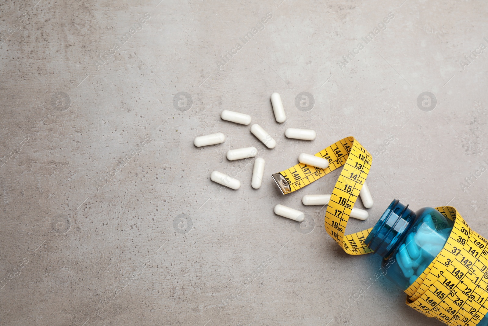 Photo of Jar of weight loss pills and measuring tape on grey table, flat lay. Space for text