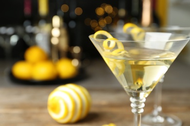 Photo of Glass of Lemon Drop Martini cocktail with zest on table against blurred background, closeup. Space for text