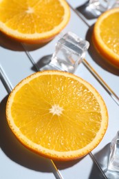 Slices of juicy orange and ice cubes on light blue background, closeup