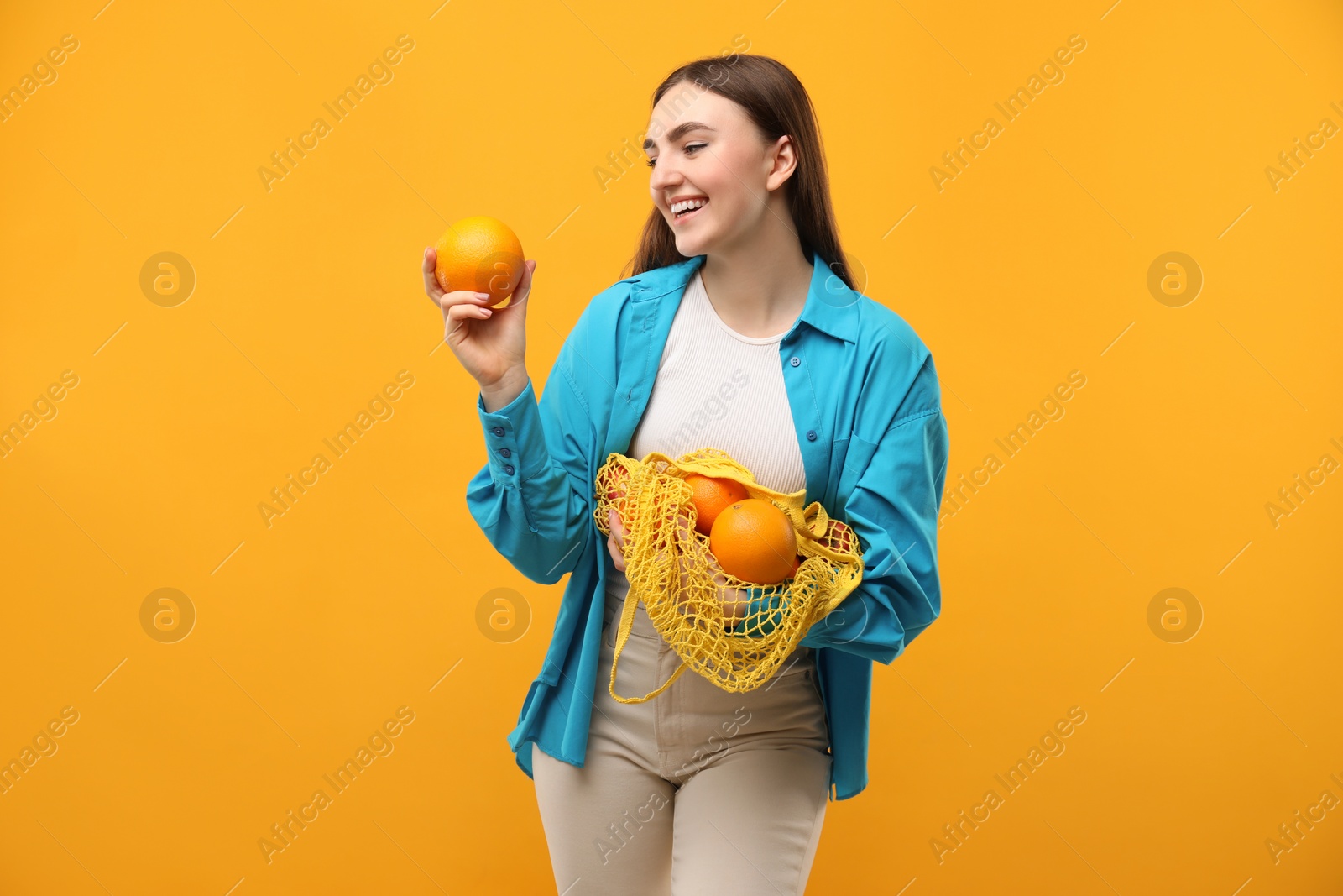 Photo of Woman with string bag of fresh oranges on orange background