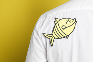 Photo of Man with paper fish sticker on back against yellow background, closeup. April fool's day