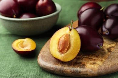 Many tasty ripe plums and wooden board on green fabric, closeup