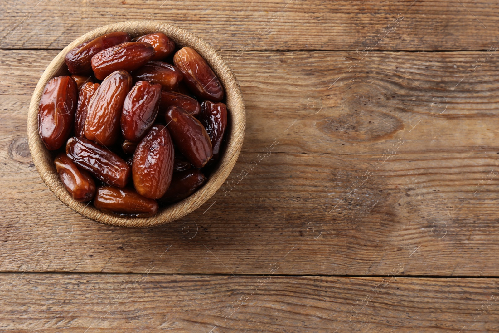 Photo of Sweet dried dates in bowl on wooden background, top view. Space for text