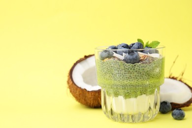 Photo of Tasty chia matcha pudding with coconut and blueberries on yellow background, space for text. Healthy breakfast