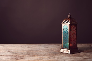 Photo of Muslim lamp with candle on wooden table. Fanous as Ramadan symbol