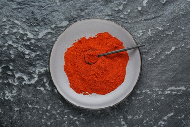 Plate of aromatic paprika on black textured table, top view