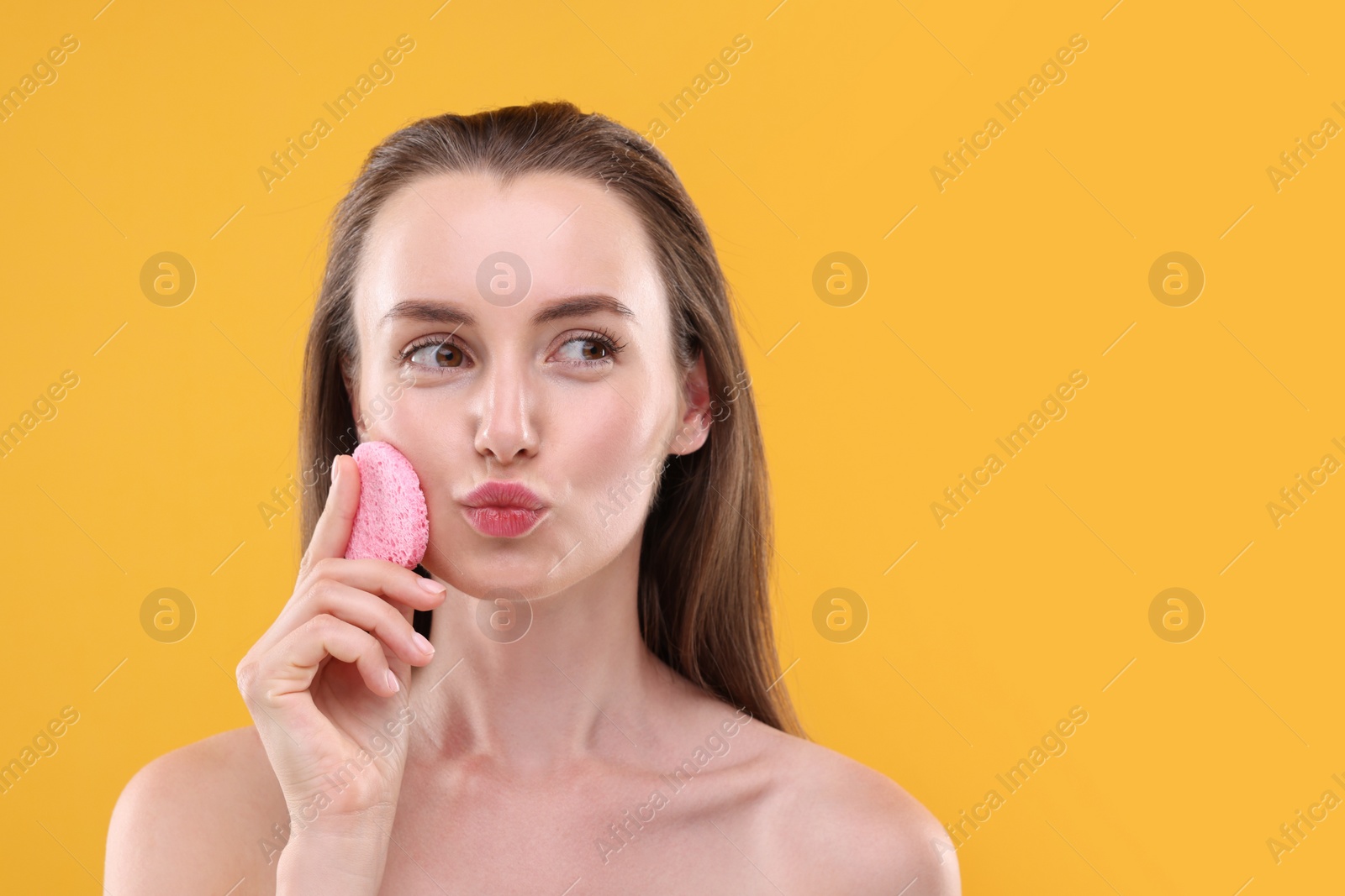 Photo of Happy young woman washing her face with sponge on orange background. Space for text
