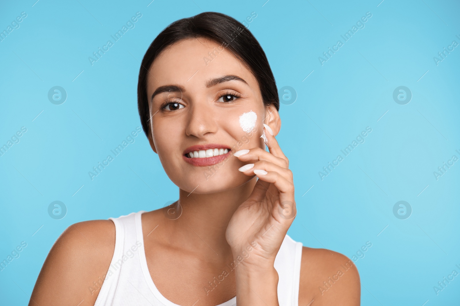 Photo of Young woman applying facial cream on light blue background