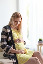 Beautiful pregnant woman sitting in light room at home