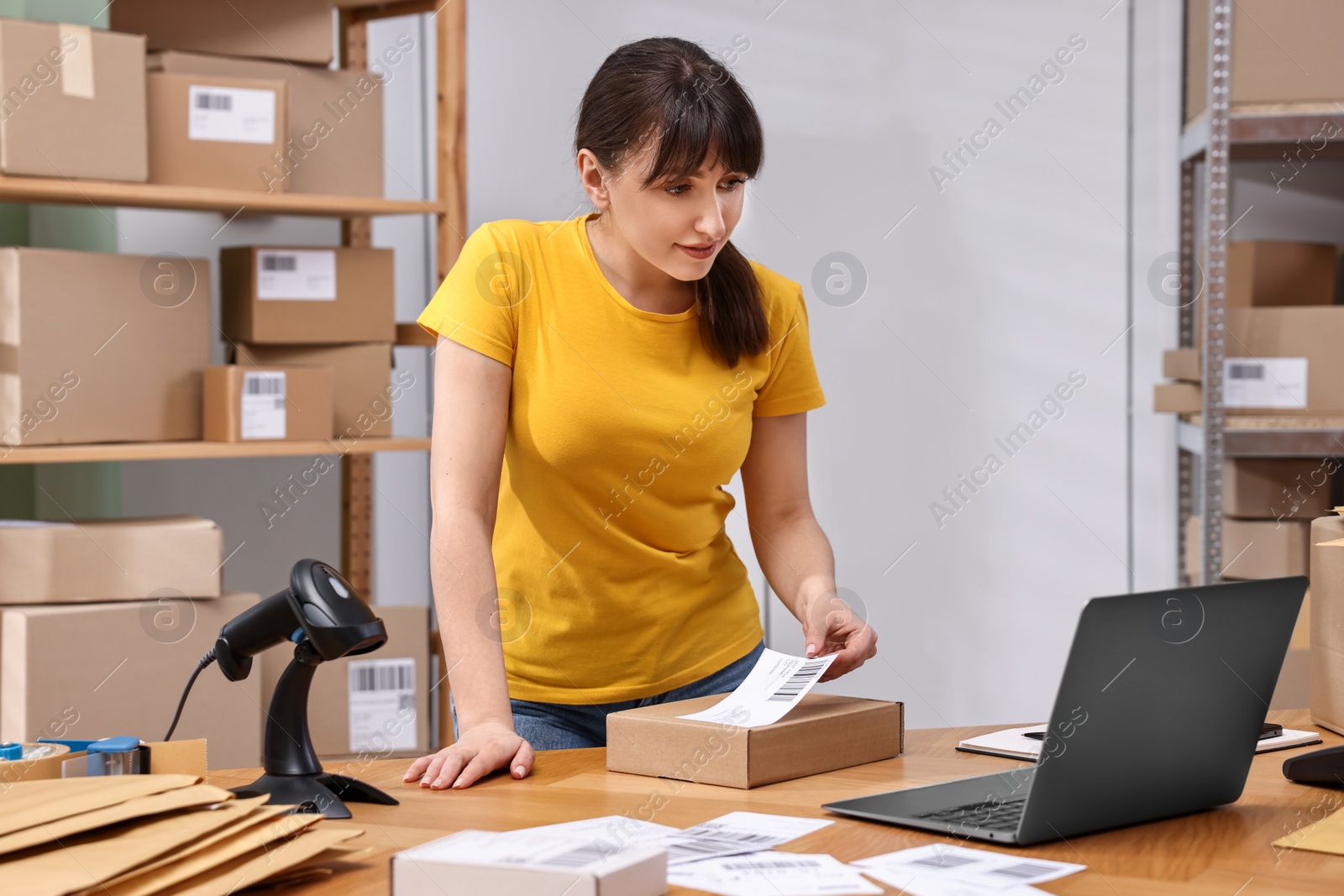 Photo of Parcel packing. Post office worker sticking barcode on box at wooden table indoors