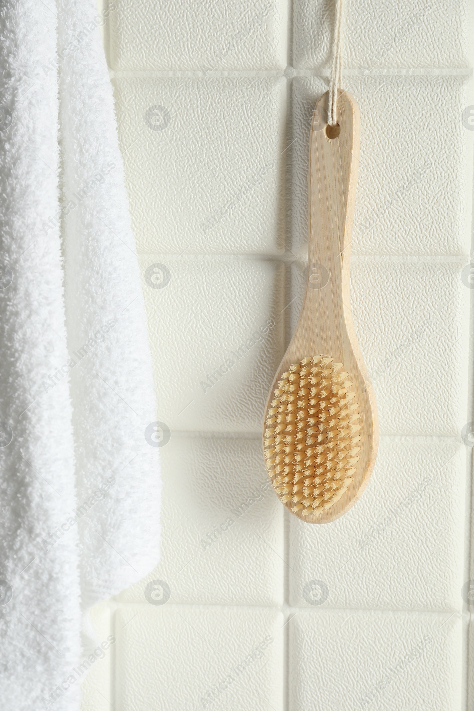 Photo of Bath accessories. Bamboo brush and terry towel on white tiled wall