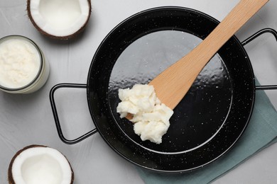 Photo of Frying pan with coconut oil and wooden spatula on light grey table, flat lay