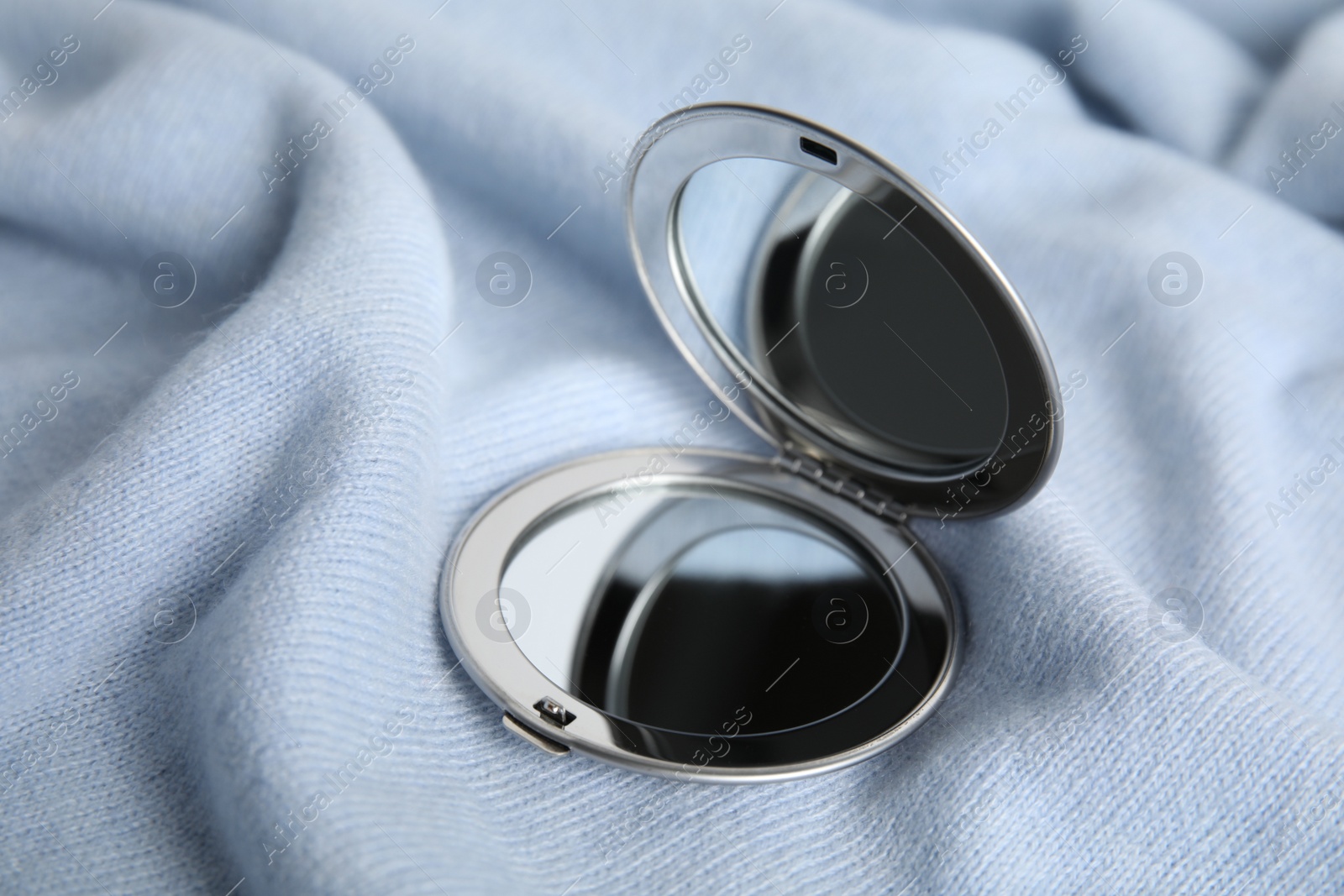 Photo of Stylish cosmetic pocket mirror on light blue fabric
